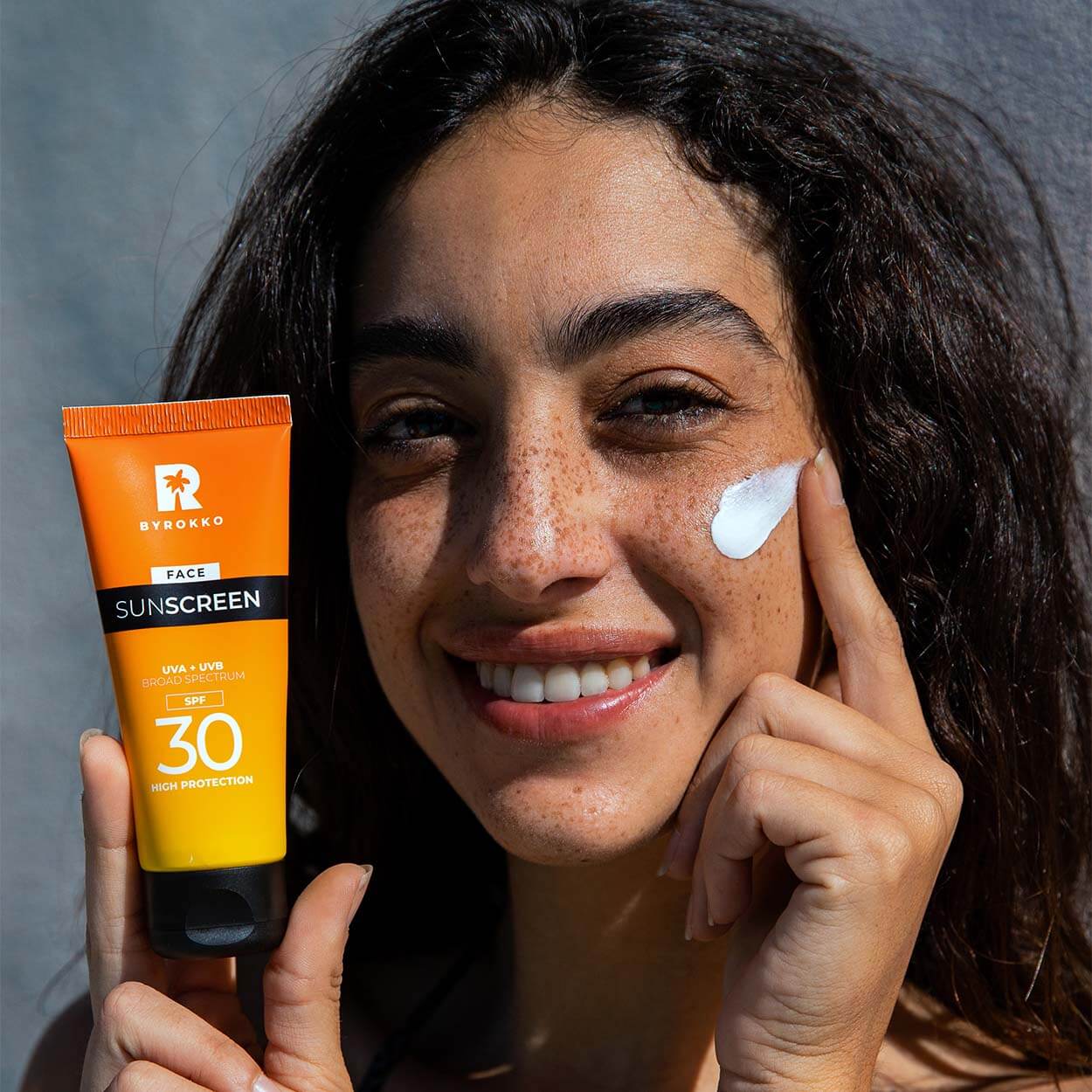 A girl with freckles is applying Byrokko Face sunscreen with SPF 30.