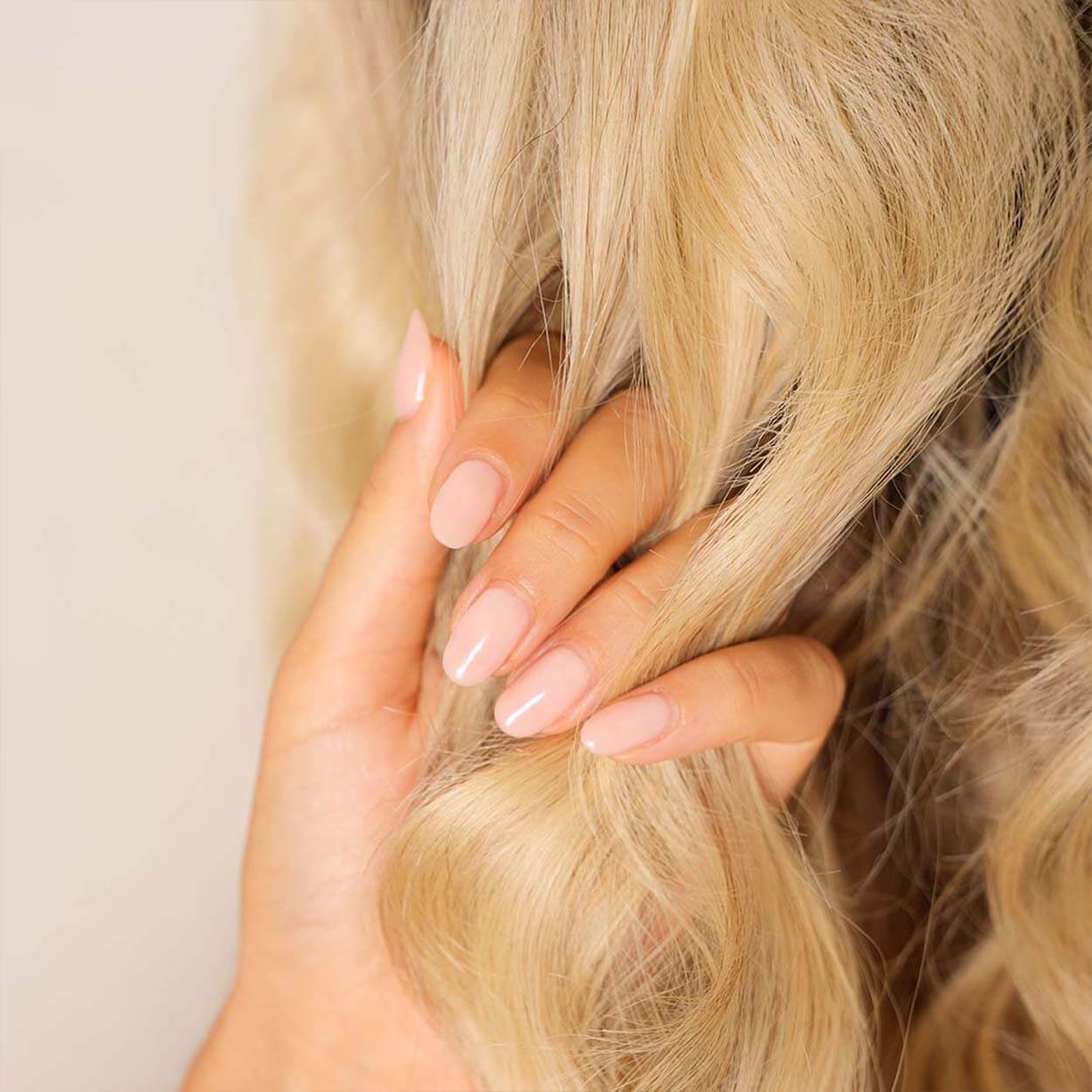 A blonde woman is applying Byrokko Coconut Bomb hair oil on her hair.